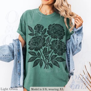 May include: Light green t-shirt featuring a black floral print. The shirt has a crew neck and short sleeves. The text "OLD SCHOOL CULT" is visible in the lower right corner. The text "Light Green" and "Model is 5'8, wearing XL" are also visible.