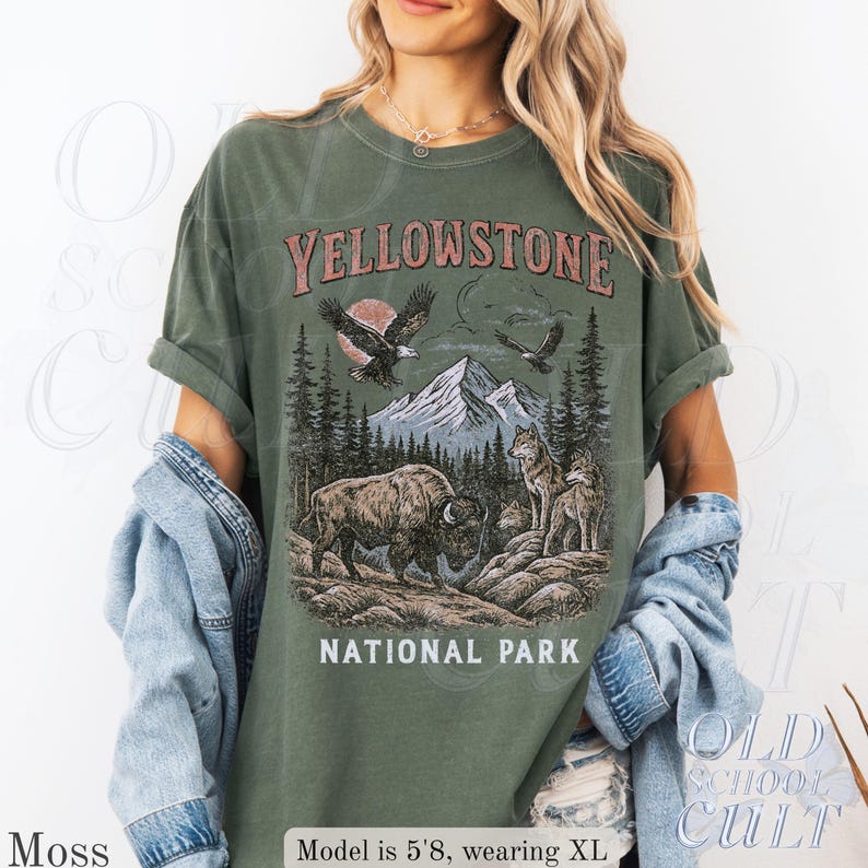 May include: Moss green t-shirt with a vintage-style Yellowstone National Park graphic. The design features a bison, wolves, eagles, mountains, and the text "YELLOWSTONE NATIONAL PARK". The shirt is a relaxed fit.