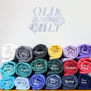 May include: A display of rolled-up fabric in various colors, including white, grey, black, yellow, purple, red, and blue. Each roll is labeled with its color name, such as "White," "Grey," and "Pepper." The text "OLD SCHOOL CULT" is displayed above the rolls.