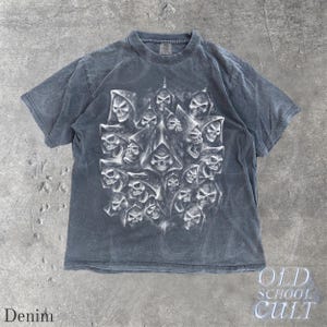 以下が含まれることがあります： デニムカラーの半袖Tシャツ。フード付きの複数のスカルのグラフィックが詳細に描かれています。クルーネックで、色あせたヴィンテージ感があります。「OLD SCHOOL CULT」の文字が右下にプリントされています。