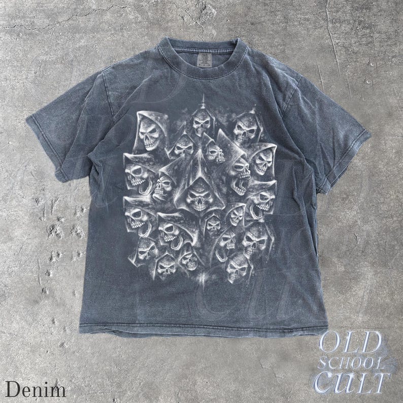 以下が含まれることがあります： デニムカラーの半袖Tシャツ。フード付きの複数のスカルのグラフィックが詳細に描かれています。クルーネックで、色あせたヴィンテージ感があります。「OLD SCHOOL CULT」の文字が右下にプリントされています。
