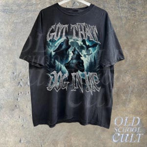 K&ouml;nnte beinhalten: Schwarzes T-Shirt mit einem Grafikdruck von W&ouml;lfen, die zum Mond heulen. Der Text "GOT THAT DOG IN ME" ist in silbernem Glitzer auf der Vorderseite des Shirts gedruckt.