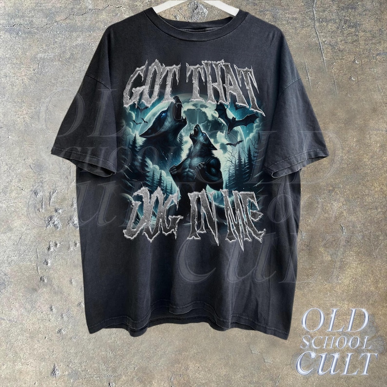 K&ouml;nnte beinhalten: Schwarzes T-Shirt mit einem Grafikdruck von W&ouml;lfen, die zum Mond heulen. Der Text "GOT THAT DOG IN ME" ist in silbernem Glitzer auf der Vorderseite des Shirts gedruckt.
