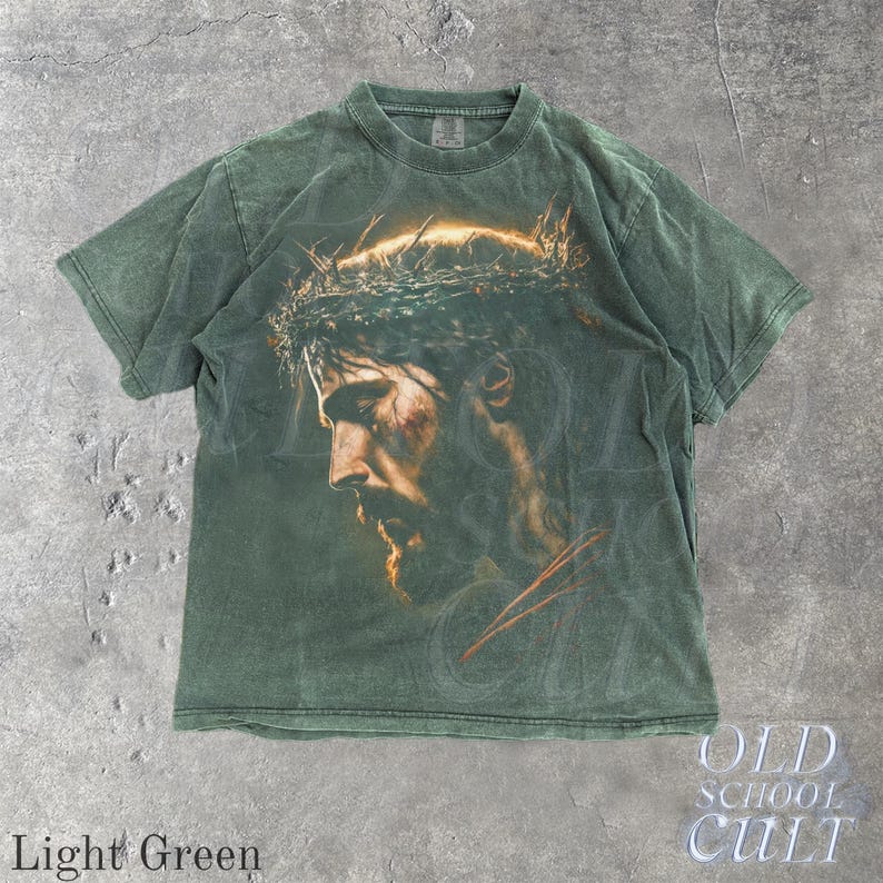 May include: Light green t-shirt featuring a detailed portrait of a man with a crown of thorns. The image is printed on the front of the shirt. The words "OLD SCHOOL CULT" are printed on the bottom right corner. The words "Light Green" are printed on the bottom left corner.