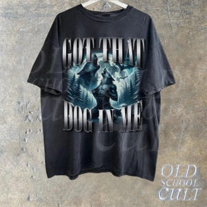 May include: A black t-shirt with a graphic print of two wolves howling at the moon. The text "GOT THAT DOG IN ME" is printed in silver lettering on the front of the shirt.