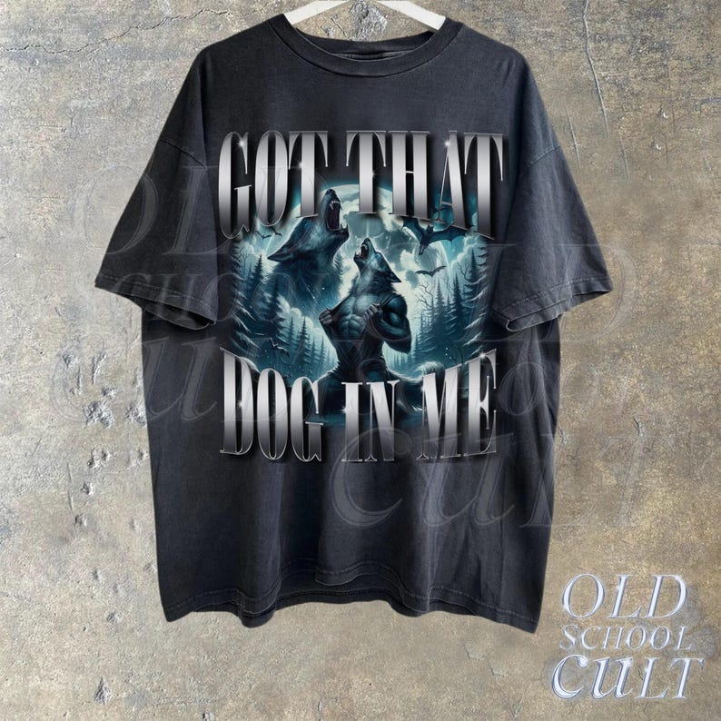 May include: A black t-shirt with a graphic print of two wolves howling at the moon. The text "GOT THAT DOG IN ME" is printed in silver lettering on the front of the shirt.