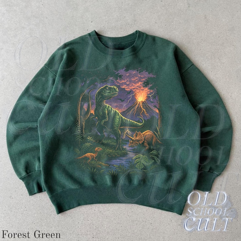 Op de afbeelding: Bostgroene sweatshirt met een dinosaurussc&egrave;ne, waaronder een T-Rex, Triceratops en vulkaan. De afbeelding toont een prehistorisch landschap. De tekst "OLD SCHOOL CULT" is rechtsonder zichtbaar.