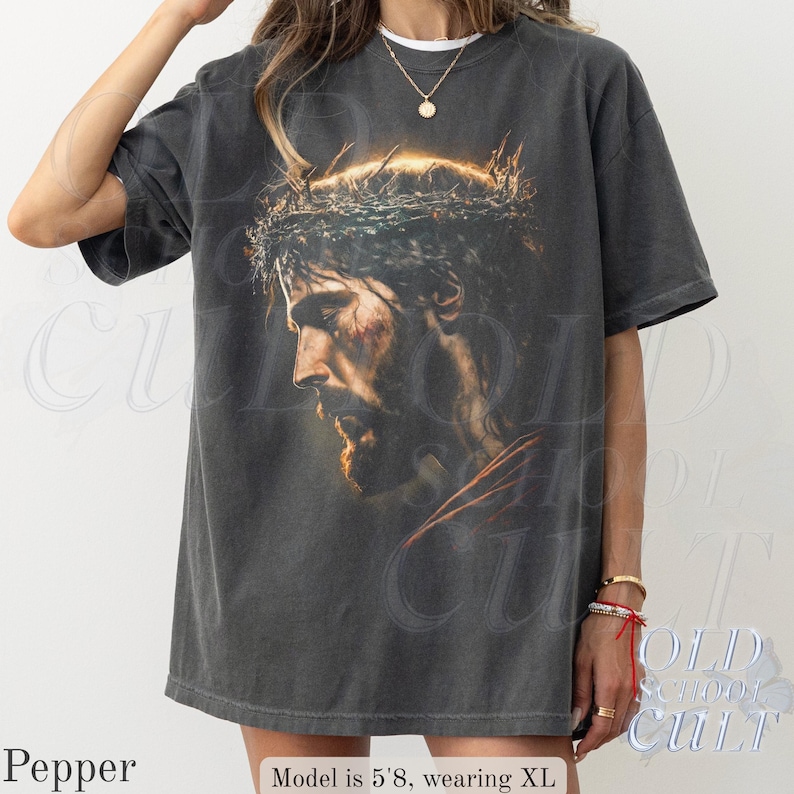 May include: A dark gray t-shirt featuring a detailed portrait of a man with a crown of thorns. The image is a side profile with a warm color palette. The text "OLD SCHOOL CULT" is visible in the background.