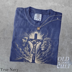May include: A navy blue t-shirt with a graphic of Jesus on the cross, flanked by a lion and a man's face. The shirt has the words "OLD SCHOOL CULT" and "True Navy" printed on it. A gold necklace with a pendant is on the shirt.