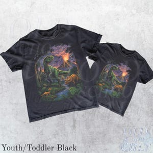 Op de afbeelding: Twee zwarte t-shirts met een dinosaurusafbeelding. Het ontwerp toont een groene Tyrannosaurus Rex, andere dinosaurussen, een rivier en een vulkaan onder een zonsonderganghemel. De tekst "Youth/Toddler Black" staat onderaan.