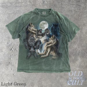 May include: Light green t-shirt featuring a detailed graphic of wolves under a full moon. The design includes various wolf poses, with the text "OLD SCHOOL CULT" at the bottom. The shirt is a light green color.