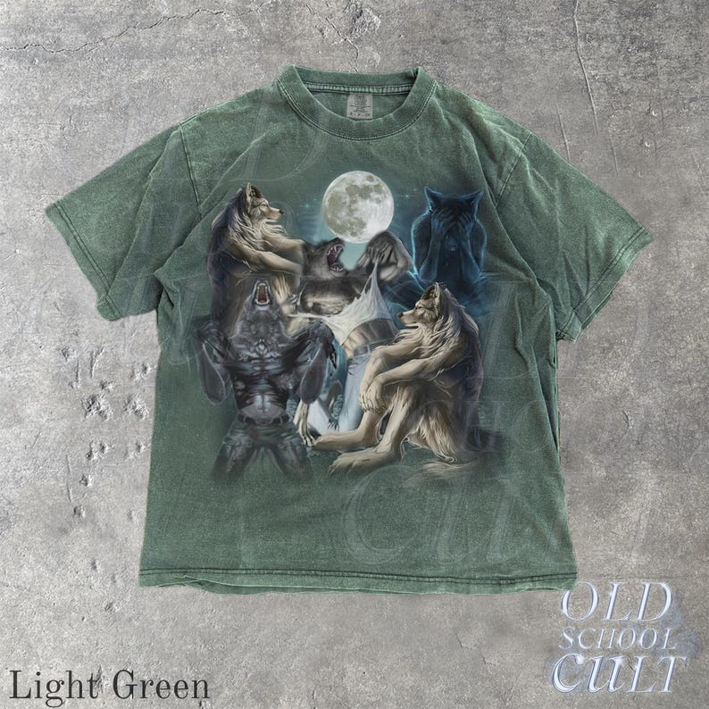 May include: Light green t-shirt featuring a detailed graphic of wolves under a full moon. The design includes various wolf poses, with the text "OLD SCHOOL CULT" at the bottom. The shirt is a light green color.