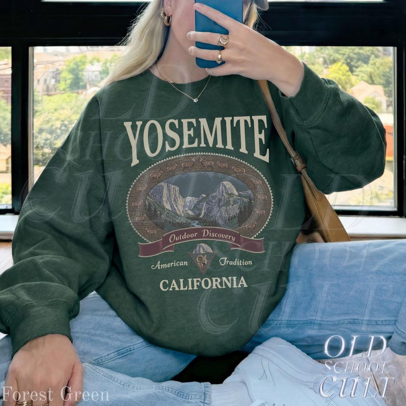 May include: Forest green sweatshirt with a Yosemite National Park graphic. The design includes the word "YOSEMITE" above an oval illustration of mountains and trees, with the words "Outdoor Discovery", "American Tradition", and "California".