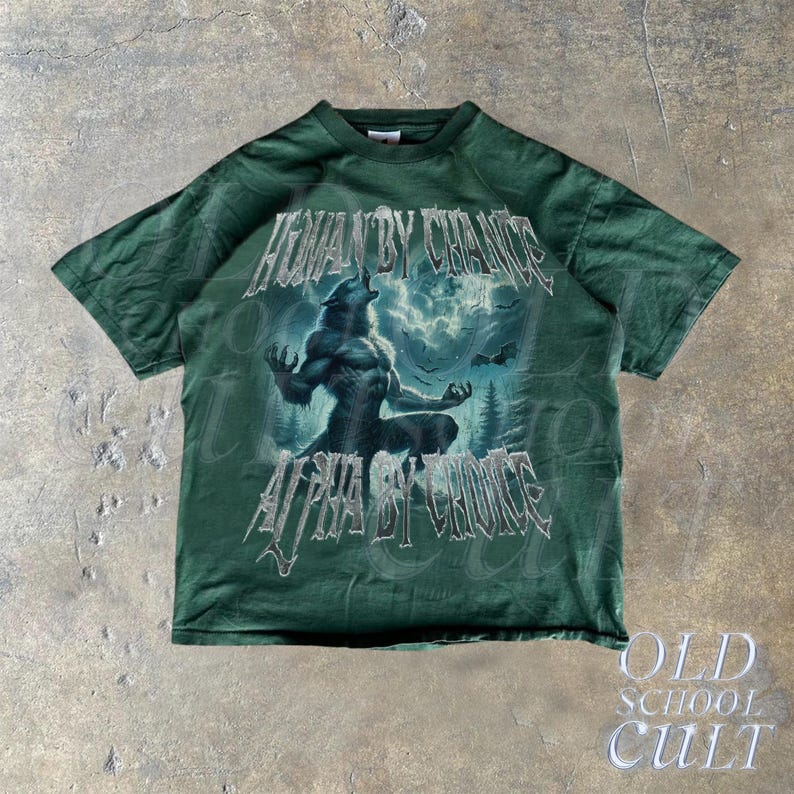 Puede incluir: Camiseta verde oscuro con un gr&aacute;fico de hombre lobo y el texto "HUMAN BY CHANCE, ALPHA BY CHOICE". El dise&ntilde;o incluye un lobo aullando a la luna, sobre un fondo de bosque. La camiseta tiene una est&eacute;tica vintage.
