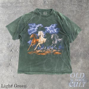 May include: Light green t-shirt featuring a graphic of four running horses under a stormy sky. The horses are in shades of brown, white, black, and gray. The text "OLD SCHOOL CULT" is in the lower right corner.