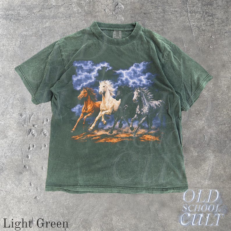 May include: Light green t-shirt featuring a graphic of four running horses under a stormy sky. The horses are in shades of brown, white, black, and gray. The text "OLD SCHOOL CULT" is in the lower right corner.