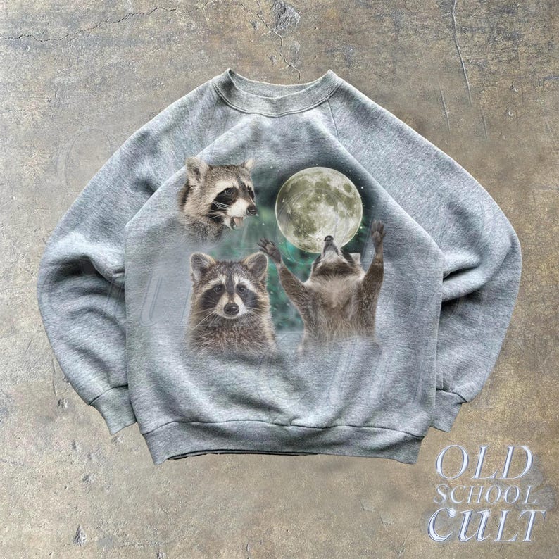 Op de afbeelding: Een grijs sweatshirt met een grafische print van drie wasberen en een maan. De wasberen staan in verschillende poses, en de maan is op de achtergrond. Het sweatshirt heeft een ronde hals en lange mouwen.