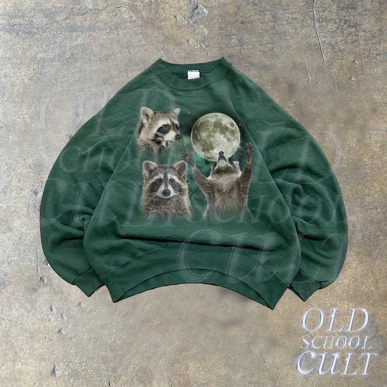 Op de afbeelding: Een donkergroen sweatshirt met een grafische print van drie wasberen die naar een volle maan kijken. De maan is lichtgroen en de wasberen zijn bruin en grijs. Het sweatshirt heeft een ronde hals en lange mouwen.