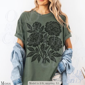 May include: A moss green t-shirt with a black floral print. The shirt has a crew neck and short sleeves. The text "OLD SCHOOL CULT" is visible on the lower right corner of the shirt.