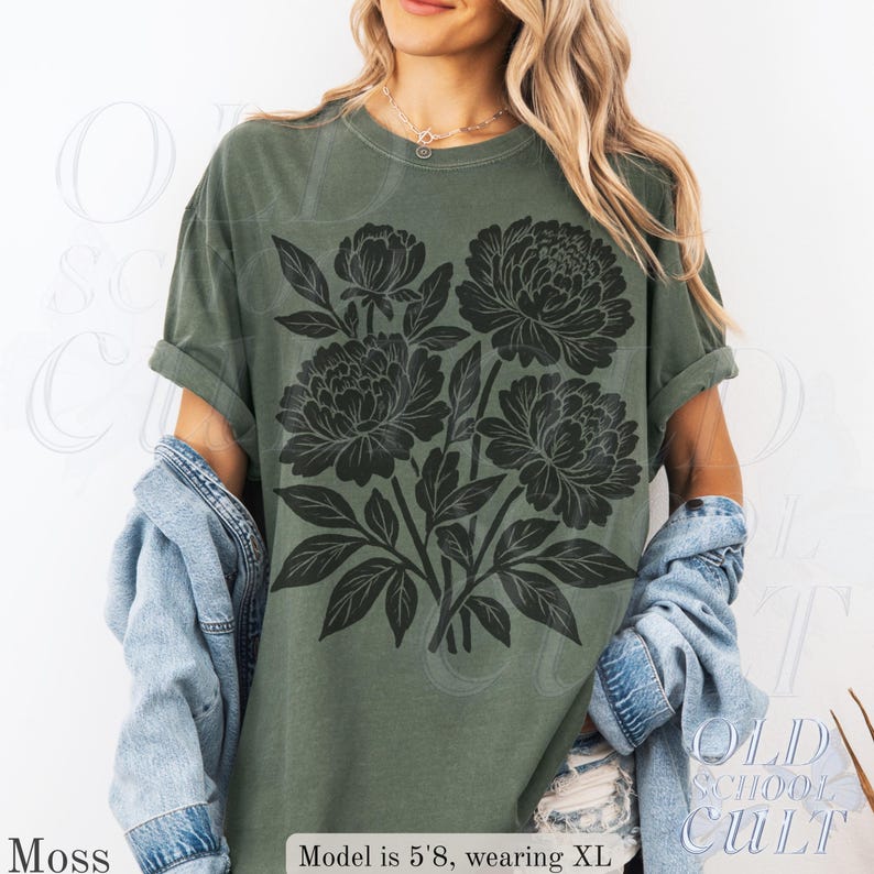 May include: A moss green t-shirt with a black floral print. The shirt has a crew neck and short sleeves. The text "OLD SCHOOL CULT" is visible on the lower right corner of the shirt.