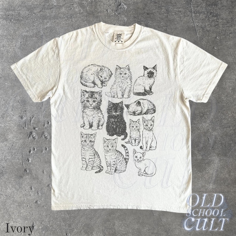 May include: Ivory-colored t-shirt featuring a collection of illustrated cats in various poses. The graphic is in black and white, with the words "OLD SCHOOL CULT" printed in a vintage style. The word "Ivory" is printed at the bottom left.