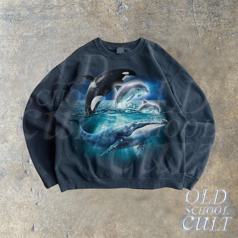 May include: Black sweatshirt with a graphic print of a whale, orca, and dolphins jumping out of the water. The graphic is in shades of blue and white.