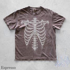 May include: Espresso-colored t-shirt featuring a detailed white illustration of a human rib cage. The shirt has a classic crew neck and short sleeves. The text "OLD SCHOOL CULT" is visible in the lower right corner.