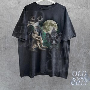 K&ouml;nnte beinhalten: Ein schwarzes T-Shirt mit einem grafischen Druck von drei Werw&ouml;lfen, die zum Mond heulen. Der Mond ist voll und hell, und die Werw&ouml;lfe sind in verschiedenen Posen. Das Shirt ist im Vintage-Stil und hat einen verblassten Look.