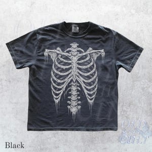 May include: Black t-shirt featuring a detailed white illustration of a human rib cage. The design is centered on the shirt, with the text "Black" at the bottom left. The shirt has a vintage, worn look.