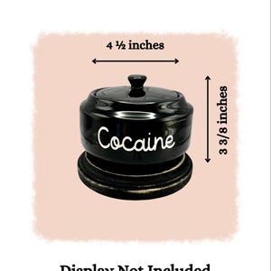 Puede incluir: Un tarro de cer&aacute;mica negro con tapa, que mide 11,4 cm de ancho y 8,6 cm de alto. La palabra "Cocaine" est&aacute; escrita en blanco en la parte delantera. El tarro se asienta sobre una base de madera oscura. "Display Not Included" est&aacute; escrito debajo.