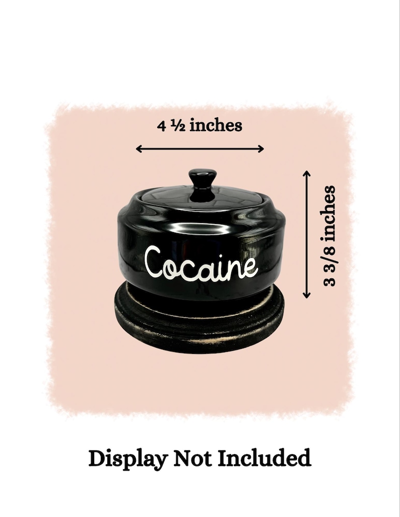 Puede incluir: Un tarro de cer&aacute;mica negro con tapa, que mide 11,4 cm de ancho y 8,6 cm de alto. La palabra "Cocaine" est&aacute; escrita en blanco en la parte delantera. El tarro se asienta sobre una base de madera oscura. "Display Not Included" est&aacute; escrito debajo.