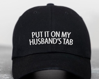 May include: Black baseball cap with white embroidered text that reads "PUT IT ON MY HUSBAND'S TAB".