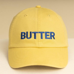 May include: A yellow baseball cap with the word "BUTTER" embroidered in blue on the front.
