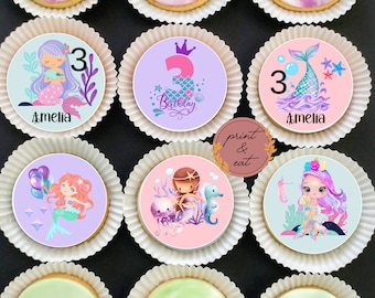 May include: Six decorated round cookies with a mermaid theme. The cookies are decorated with purple, pink, blue, and green frosting. The cookies have a mermaid, a number 3, and the name Amelia on them. The cookies are on a white background.