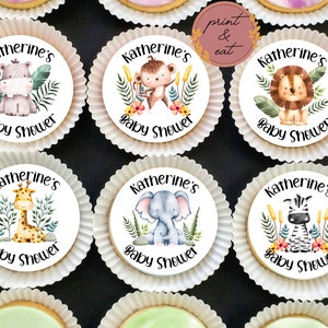 以下が含まれることがあります： ジャングル動物をテーマにした、丸い白い食べられるケーキトッパーが6つ。各トッパーには、キリン、シマウマ、ゾウ、ライオン、サル、カバなど、さまざまな動物が描かれています。トッパーは緑の葉と花で飾られています。各トッパーには「Katherine's Baby Shower」の文字が印刷されています。