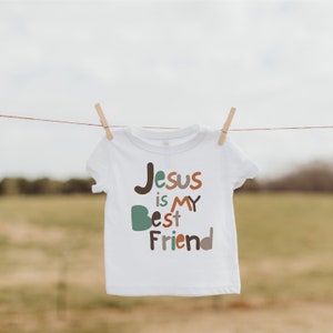 Op de afbeelding: Een witte baby romper met de tekst "Jesus is mijn beste vriend" in kleurrijke, gestileerde letters.