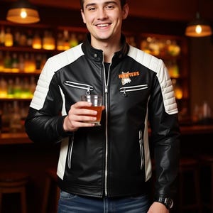 May include: Black and white leather jacket with the word "Hooters" on the chest. The jacket has white quilted shoulder panels and a zippered front. The person is holding a glass of amber liquid.