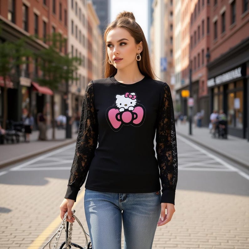 May include: Black long-sleeve shirt with a Hello Kitty graphic. The shirt features a round neck and black lace sleeves. The graphic shows Hello Kitty with a pink bow on her head, centered on a pink bow.