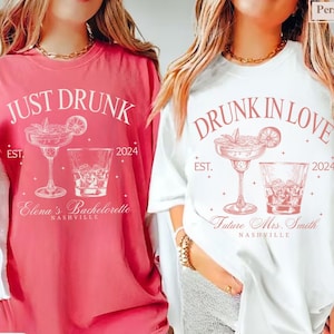 May include: Two white t-shirts with a pink design. The left shirt says "Just Drunk" with a margarita and a glass of whiskey. The right shirt says "Drunk in Love" with a margarita and a glass of whiskey. Both shirts have the year 2024 and the city Nashville.