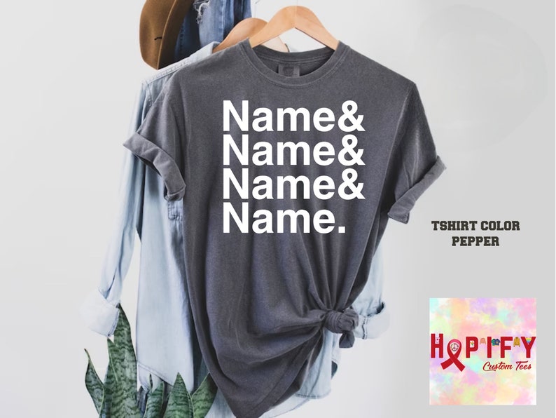 May include: A grey t-shirt with the text "Name & Name & Name & Name." printed in white. The t-shirt is on a hanger and has a knotted bottom. The text "T-shirt Color Pepper" is visible in the bottom right corner of the image.