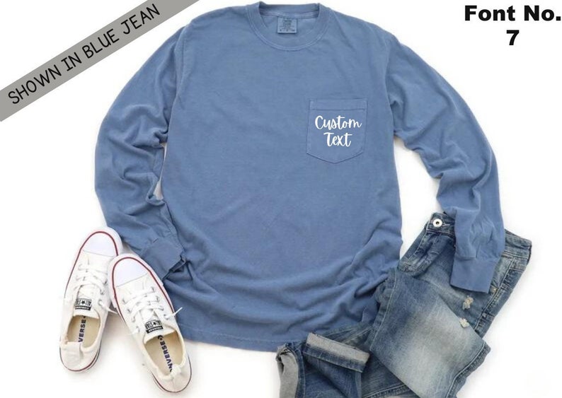 以下が含まれることがあります： 左側にポケットが付いた青い長袖Tシャツ。ポケットには「Custom Text」という白い文字が書かれています。シャツは白い背景に白いスニーカーと青いジーンズを合わせています。