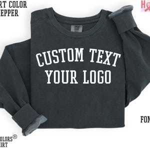 May include: A dark grey sweatshirt with the text "CUSTOM TEXT YOUR LOGO" in white. The sweatshirt is made of a soft, comfortable material and is perfect for everyday wear.