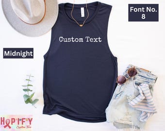 May include: A navy blue sleeveless tank top with the text "Custom Text" in white. The tank top is laying flat on a white surface with a hat, sunglasses, and denim shorts.
