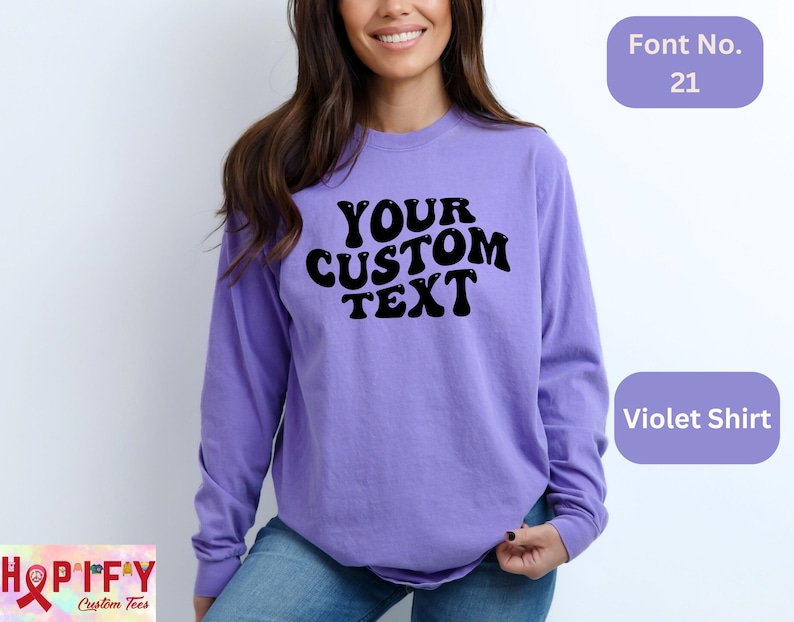 May include: A purple long-sleeve shirt with the text "YOUR CUSTOM TEXT" in a retro font. The shirt is a blank canvas for personalization.