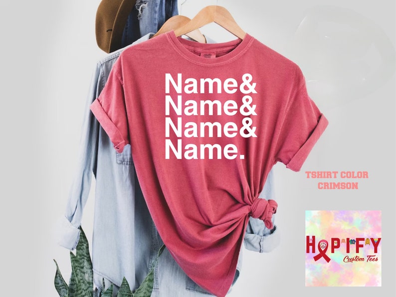 May include: A crimson t-shirt with the text "Name & Name & Name & Name." printed in white. The shirt is on a hanger and has a distressed look. The text "T-shirt Color Crimson" is visible below the shirt. The image also includes a logo for "Hopify Custom Tees" with a pink ribbon.