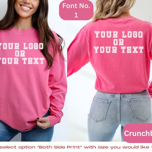 May include: A pink long-sleeved t-shirt with the text "YOUR LOGO OR YOUR TEXT" printed on the front and back. The shirt is shown on a model wearing blue jeans.