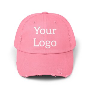 May include: Pink distressed baseball cap with the text "Your Logo" in white.