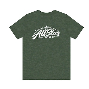 May include: A dark olive green short-sleeve t-shirt featuring a white graphic print on the chest. The design displays the text All Star CLEANING CO in a stylized script font, accompanied by a star icon and small decorative star accents above.