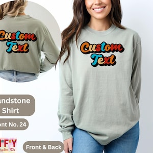 Pode incluir: Uma camiseta de manga comprida verde claro com o texto "Custom Text" em uma fonte retr&ocirc; com cores laranja, vermelho, azul e preto. A camiseta &eacute; mostrada em um modelo de frente e verso.