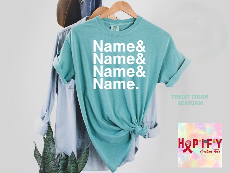 May include: A turquoise blue t-shirt with the text "Name & Name & Name & Name." printed in white. The t-shirt is on a hanger and has a knotted bottom. The text "T-shirt Colour Seafoam" is printed below the shirt.